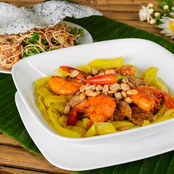 Thai-style yellow noodles topped with shrimp, meat, peanuts, and chili, served alongside fried noodles and crispy crackers.